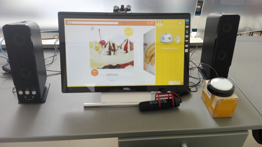 Kiosco montado con la interfaz de Nimbus y el chatbot en la pantalla táctil, junto a parlantes, micrófono y botón